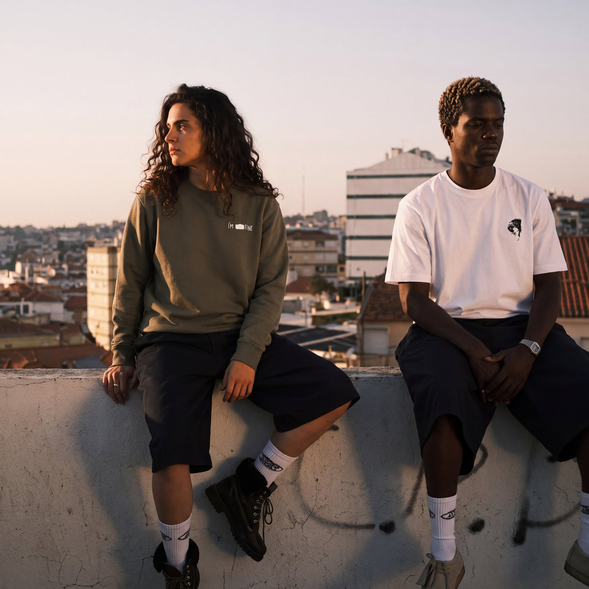 2 people, a man and a woman, sitting on a ledge wearing a white I'm fine and an Olympus t-hsirt